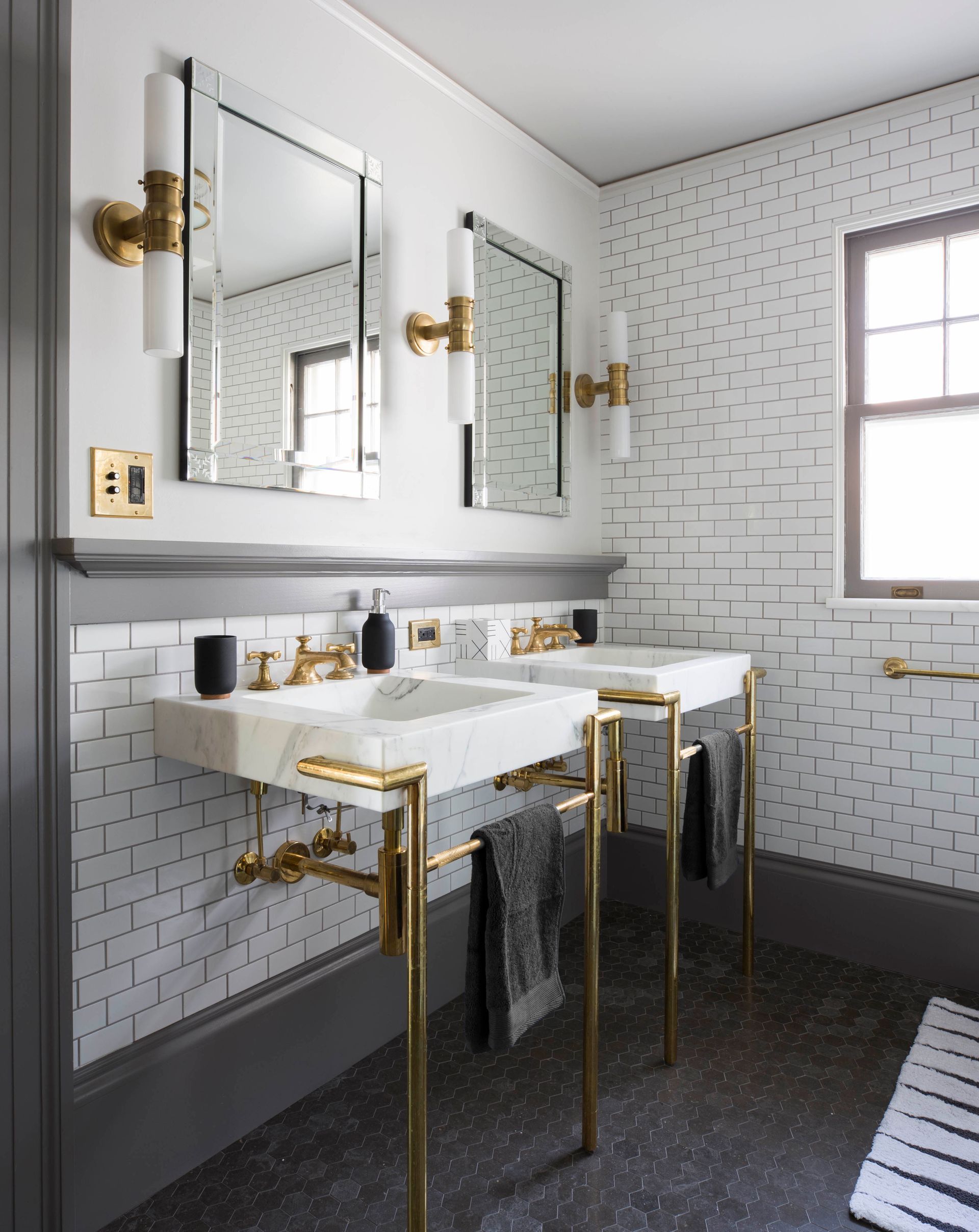 A pair of sleek, marble console sinks with brass legs, as well as brass faucets, hardware and light fixtures, strike a warm tone in this otherwise neutral vintage-inspired bath. 