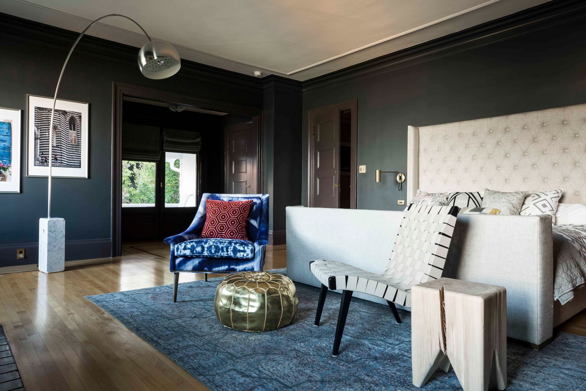 The main bedroom in a rich charcoal gray has a white upholstered bed and fun-textured furniture under an Arco lamp.
