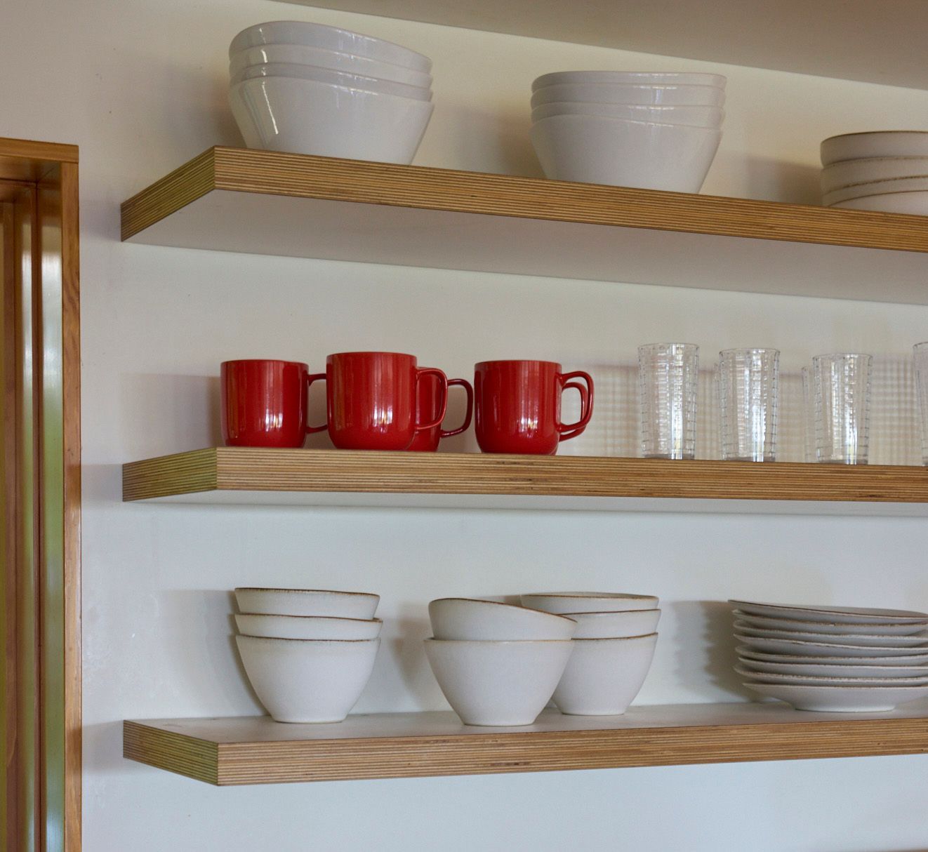 Bold floating shelves made of exposed-edge plywood hold carefully curated everyday dishware. 