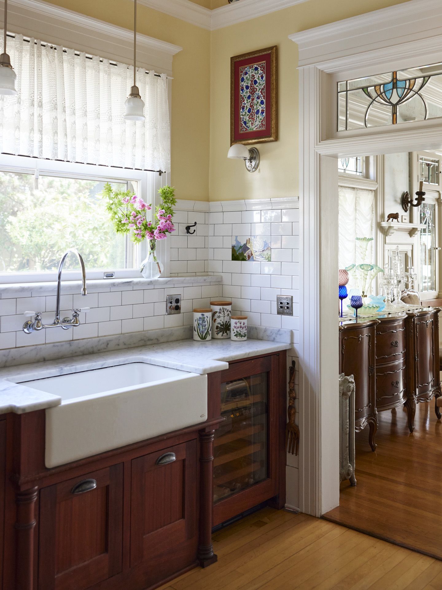 Approaching the main farmhouse sink, the doorway to the dining room to the right has a stained glass transom window above.