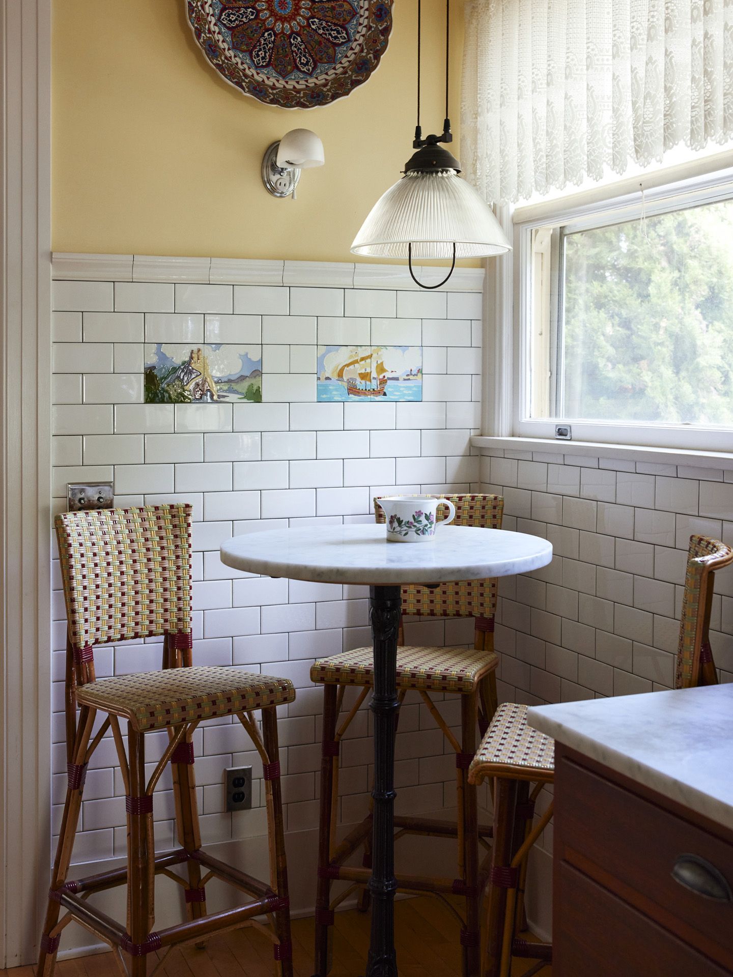 Close up of the cafe table in the kitchen corner. Original hand painted tile is surrounded by white subway tile as a wainscot and a pulley pendant offers extra illumination on dark winter days.