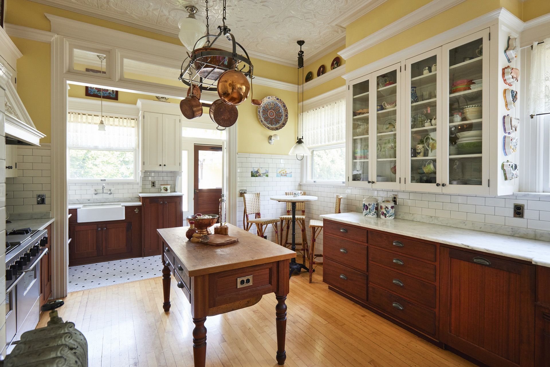 View of the sink wall and corner cafe table also shows the island, hanging pot rack and rich base cabinets.