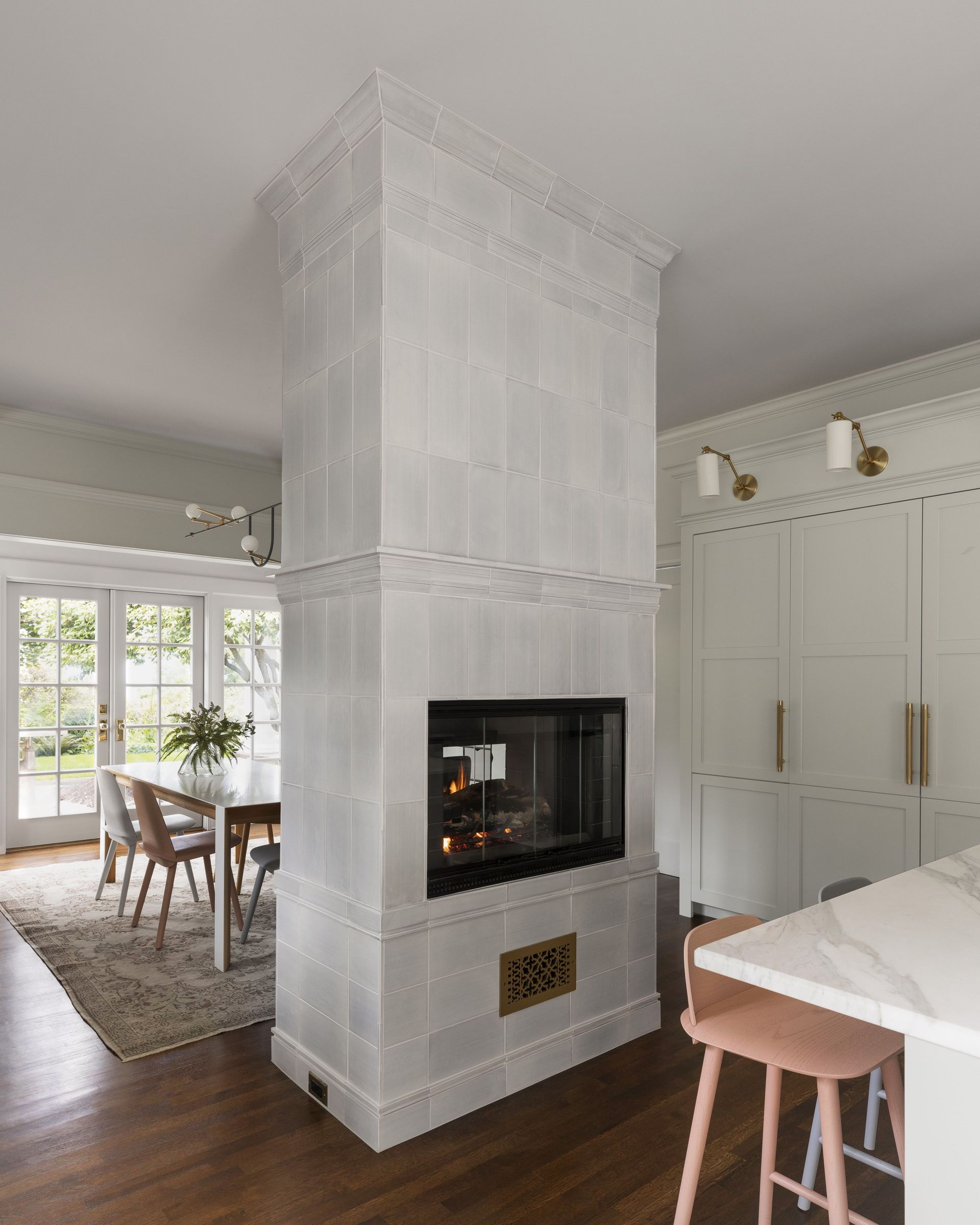 A double sided, tile-stove-inspired, gas fireplace with a casual dining table and fully integrated refrigeration beyond.