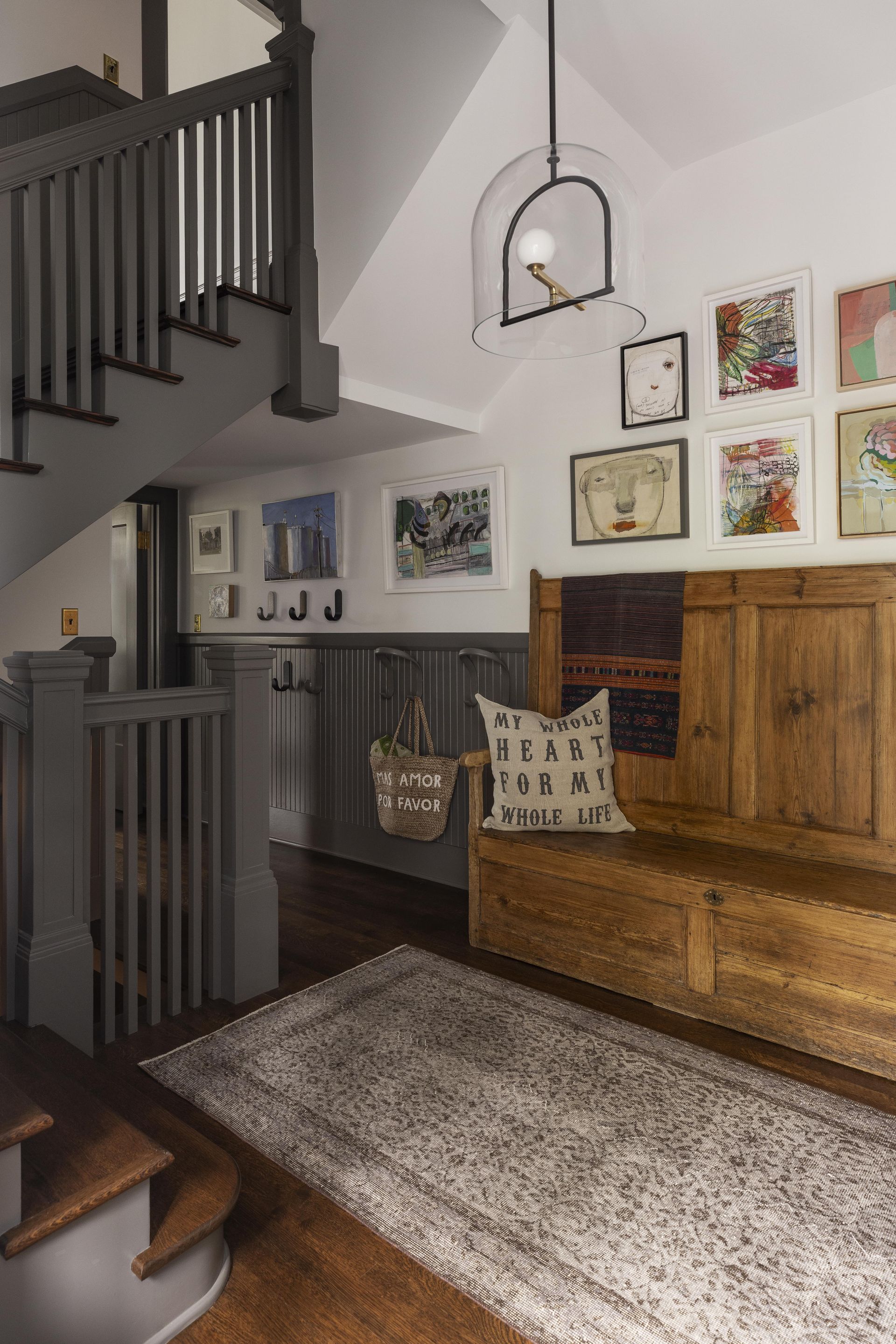 Back entry and stairs of a colonial mansion with a vintage bench and family artwork.
