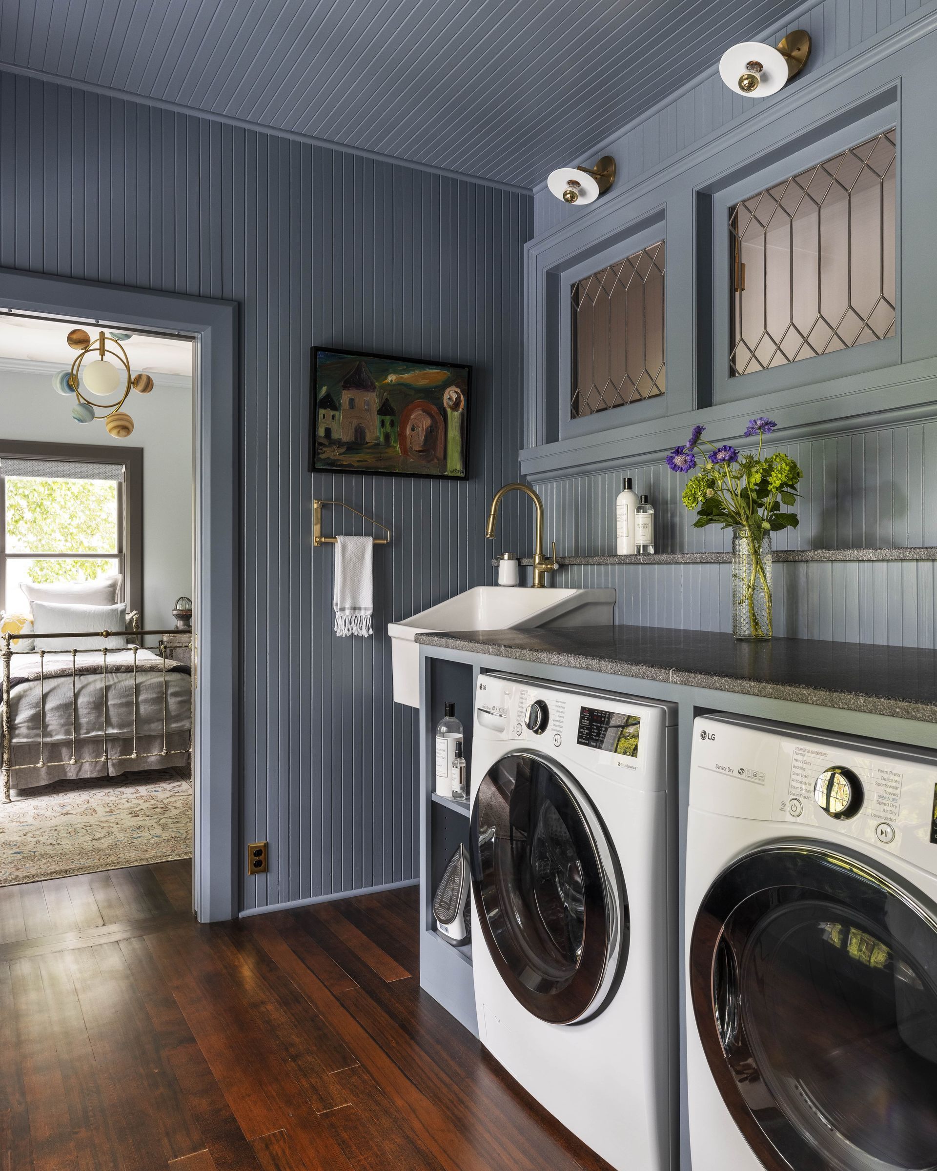 A laundry room with v-groove paneling on walls and ceiling, interior windows, wood floors and a large wall mounted sink.