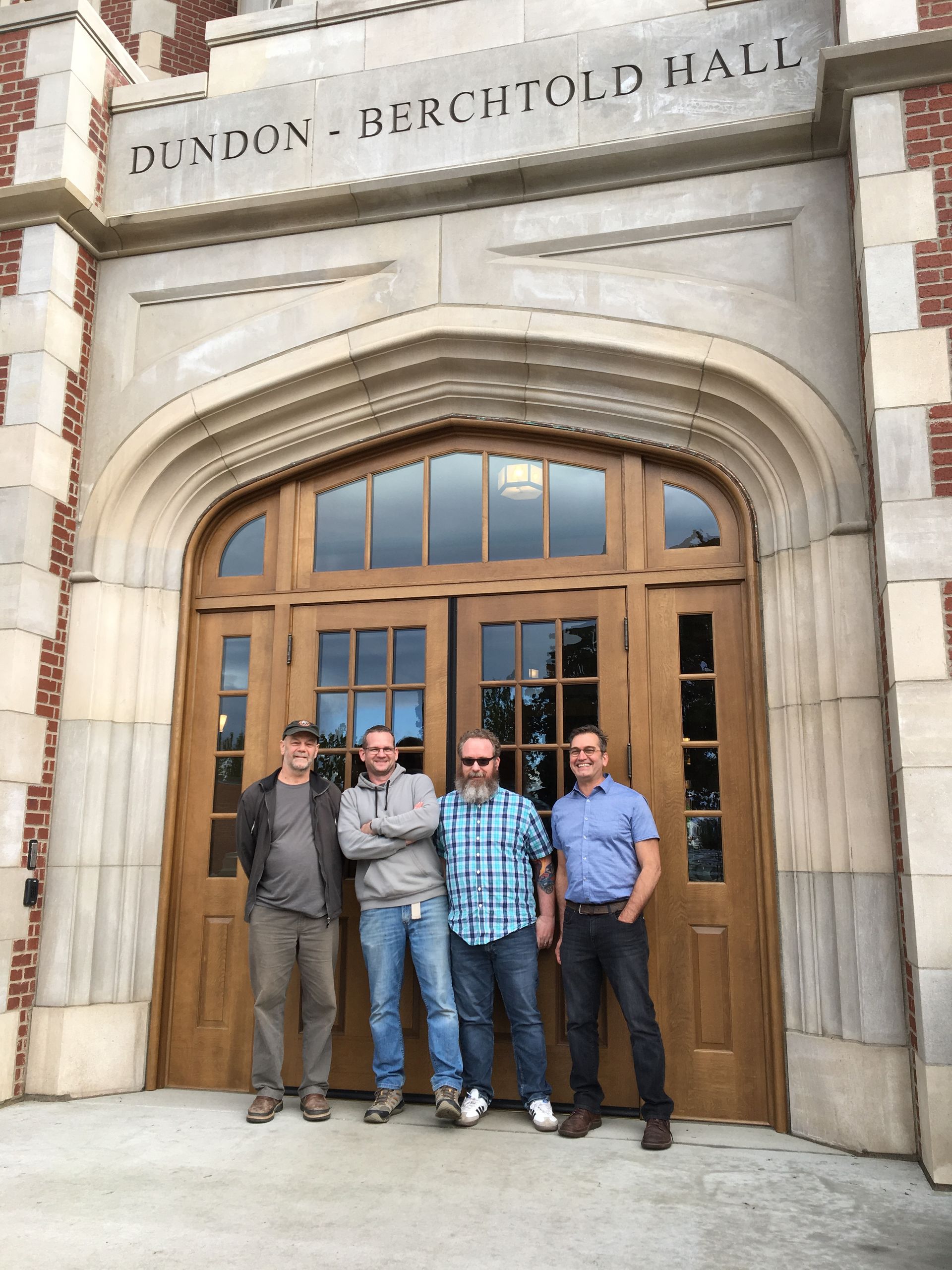 Four men standing in front of a building that says dundon-berchtold hall