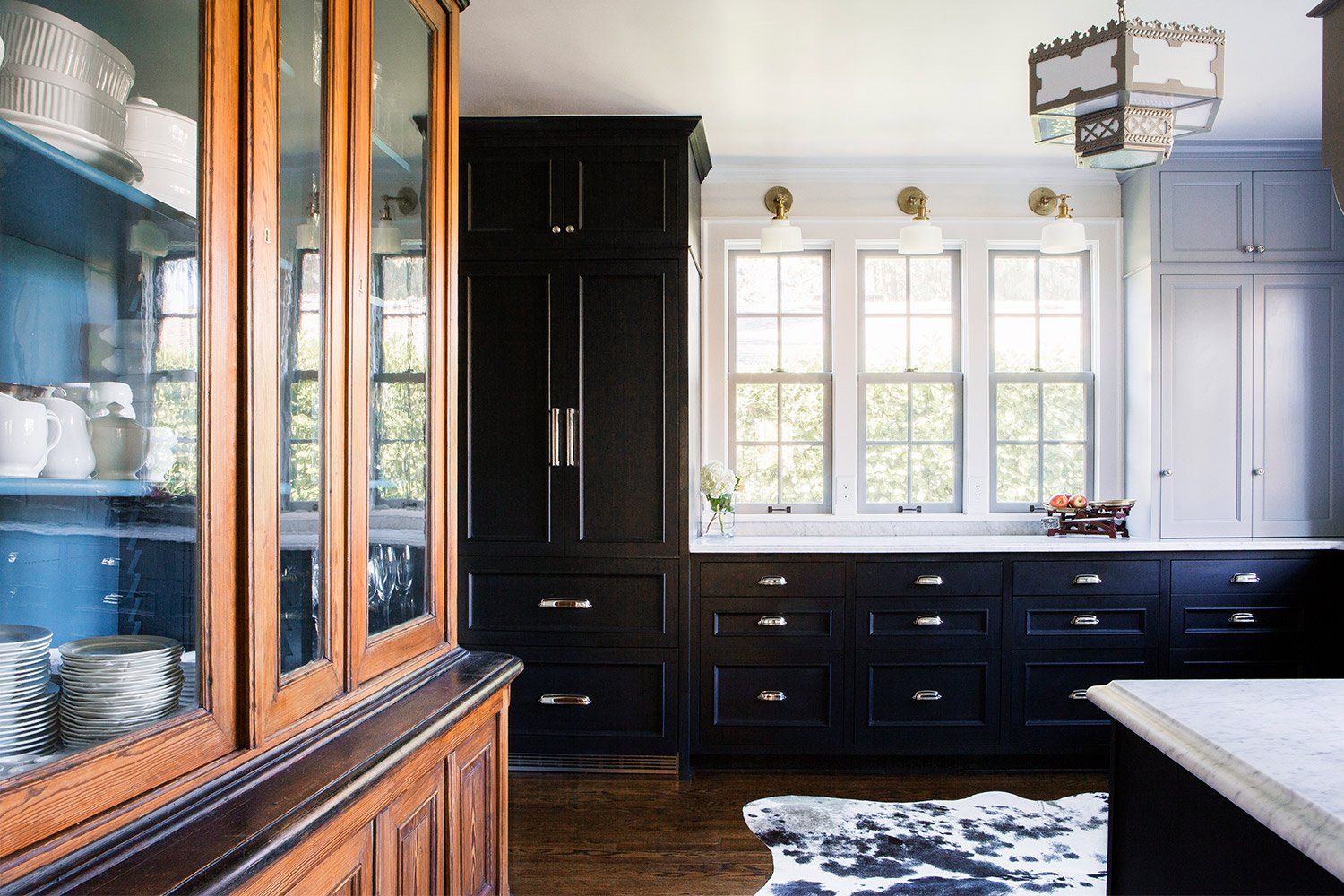 Looking into the remodeled kitchen with ebonized cabinets and plentiful windows in the background and an antique hutch at the left.