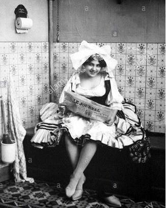 A woman in a costume is sitting on a bench holding a newspaper.
