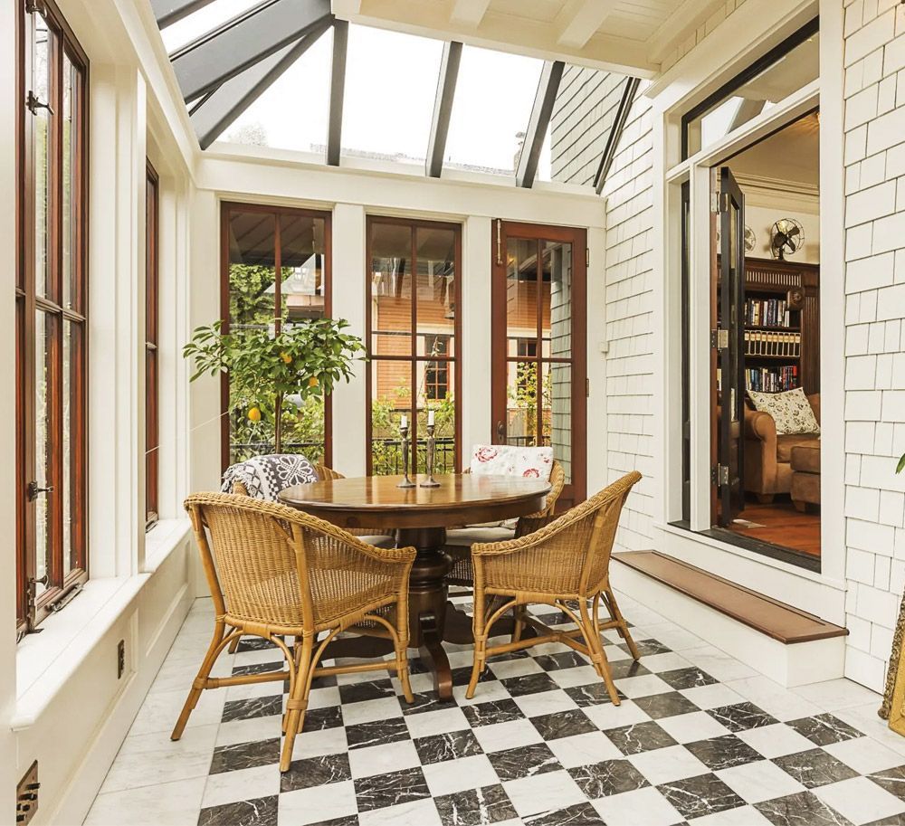 There is a table and chairs in the sunroom with a checkered floor.