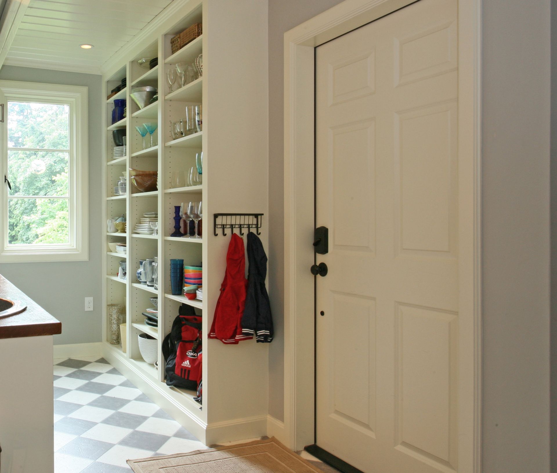 Floor-to-ceiling open shelving added to one wall of this new mudroom entry provides pantry storage for extra serving pieces, glassware, and dishes. 