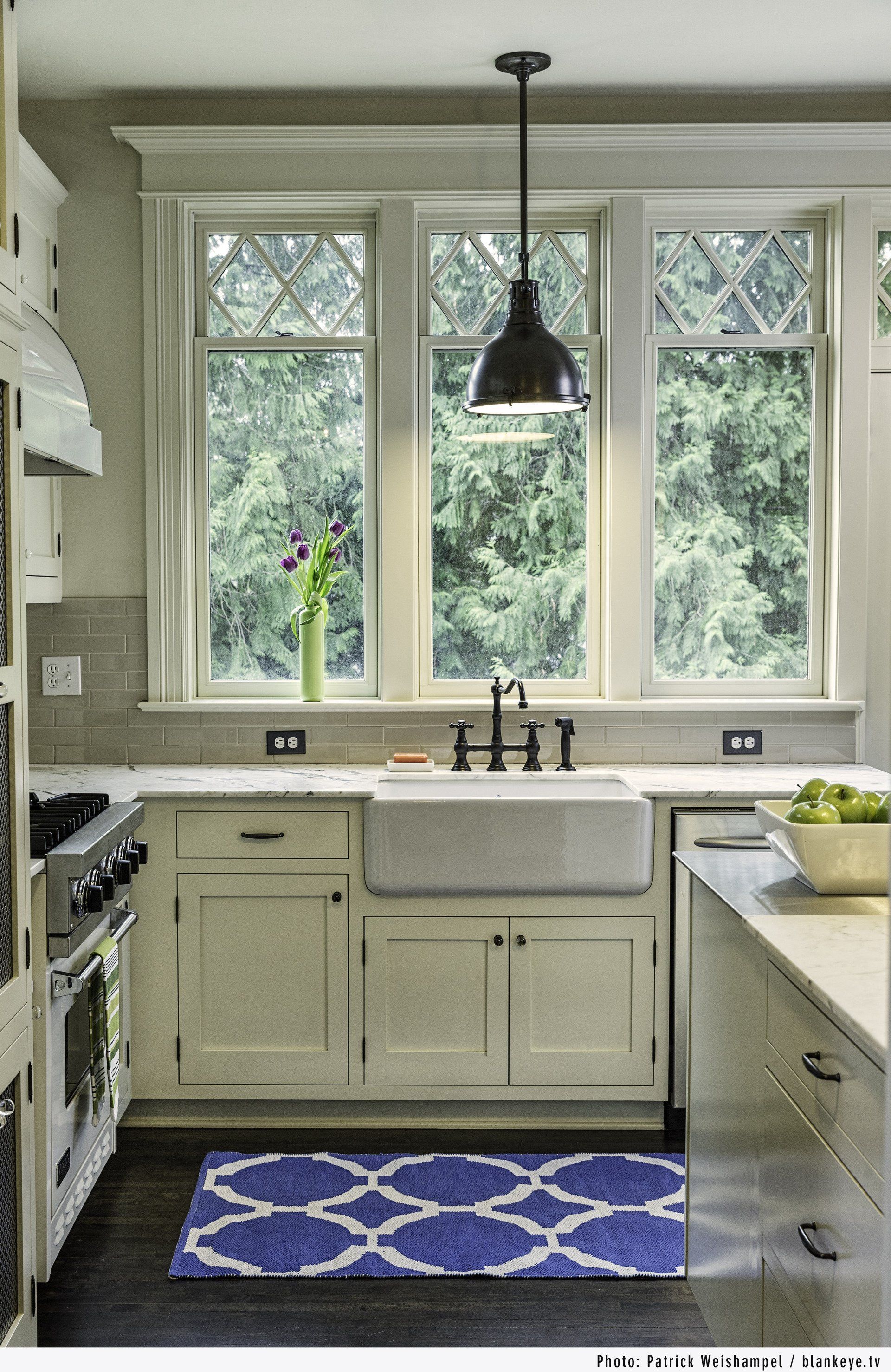 The fully remodeled kitchen - view of the sink and cabinetry under the trio of windows, with a gas range on the left.