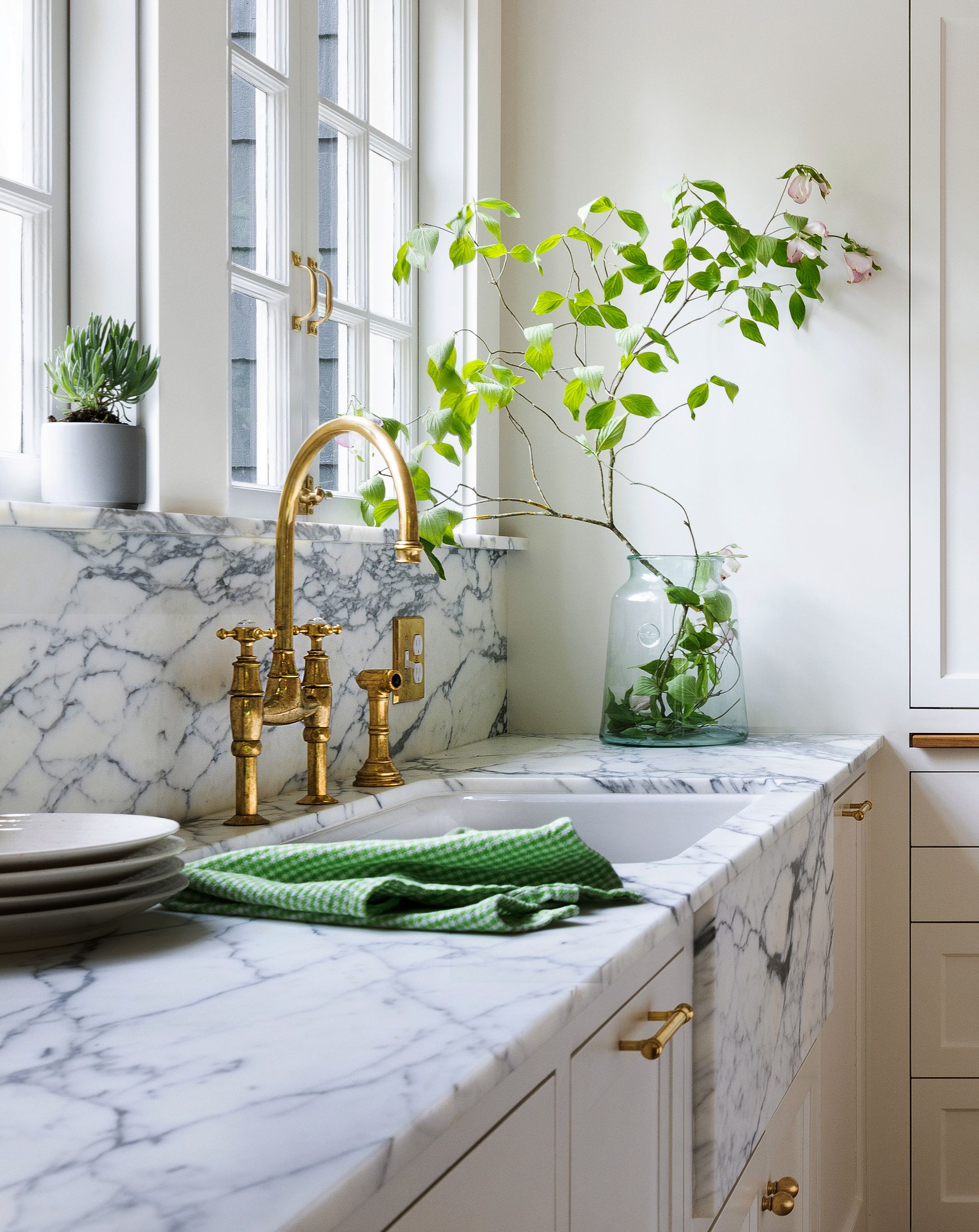 Under a generous pair of windows, the Arabescato marble counter and backsplash and the unlacquered brass faucet look beautiful in the light.