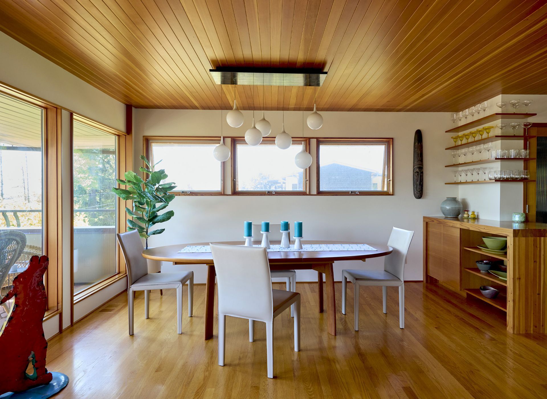 The living room opens to the dining room on the upper level. Under a tongue-and-groove vertical-grain fir ceiling is the sleek dining table with a trio of clerestory windows and a custom light fixture above.