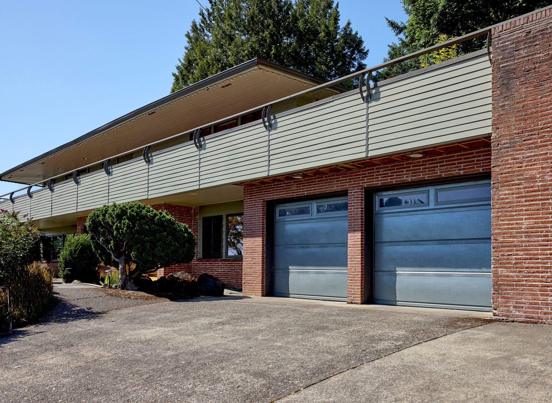 view of the front of a 1951 midcentury modern ranch home with full width balcony above the front door and garages