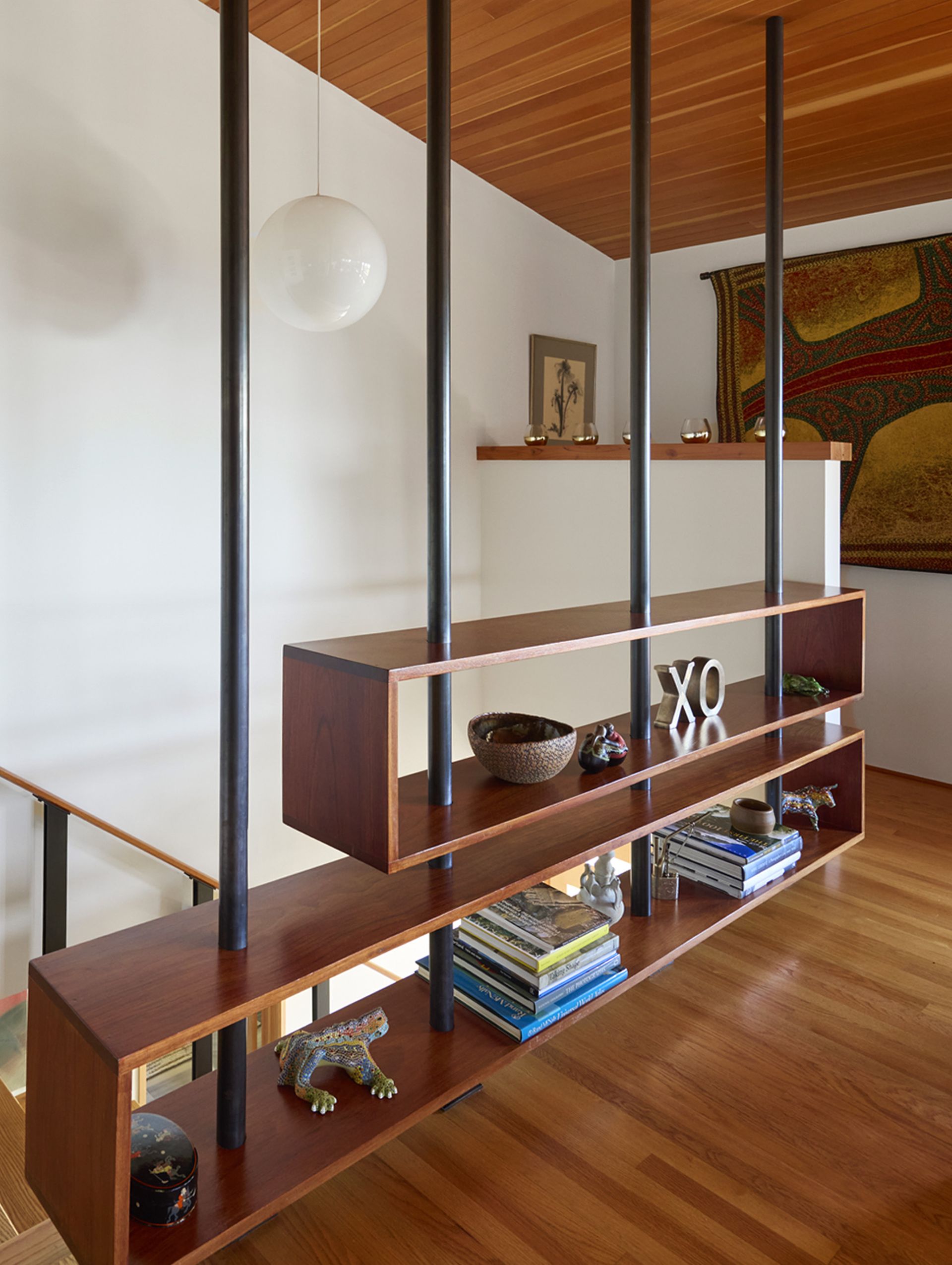The main stairs land in the spacious living room, with a custom, sculptural wood shelving unit as a divider that lets light into the stairwell.