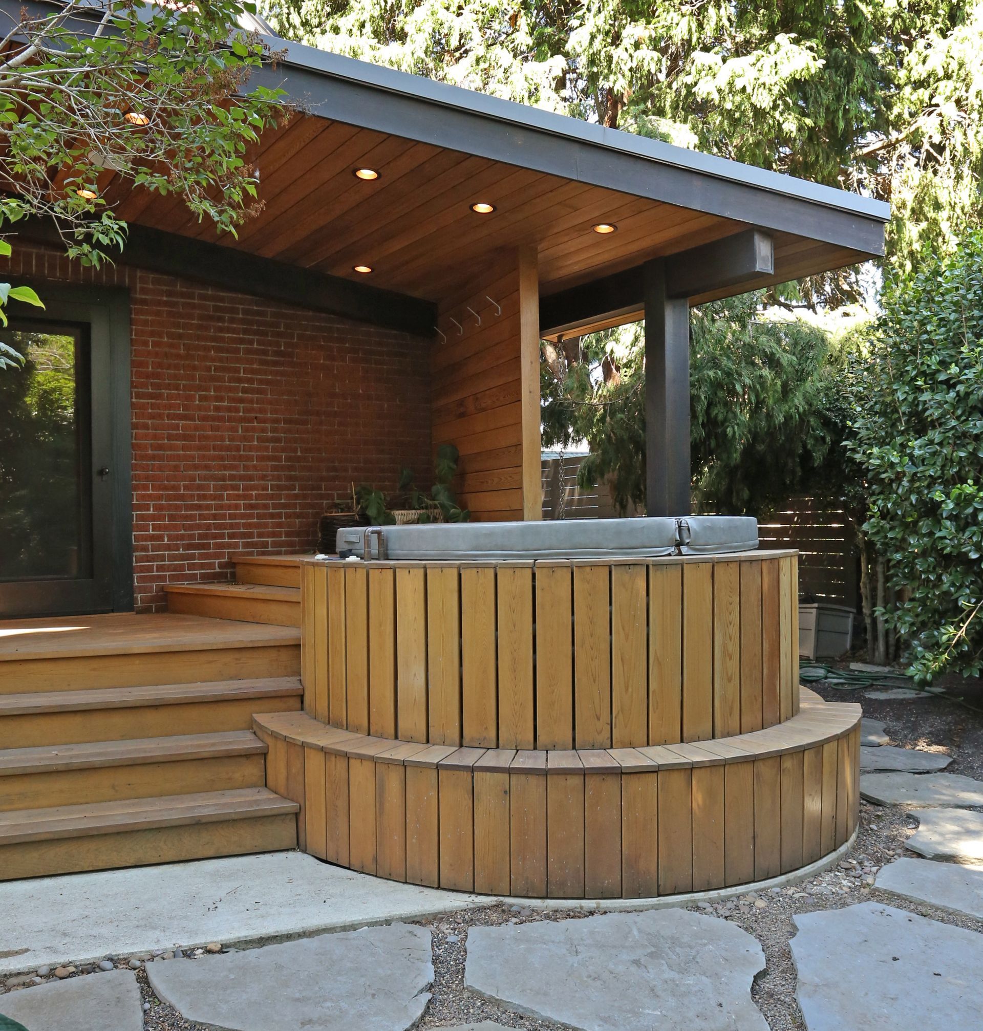 At the back of the brick home, looking at the semi-covered hot tub,  deck and stairs