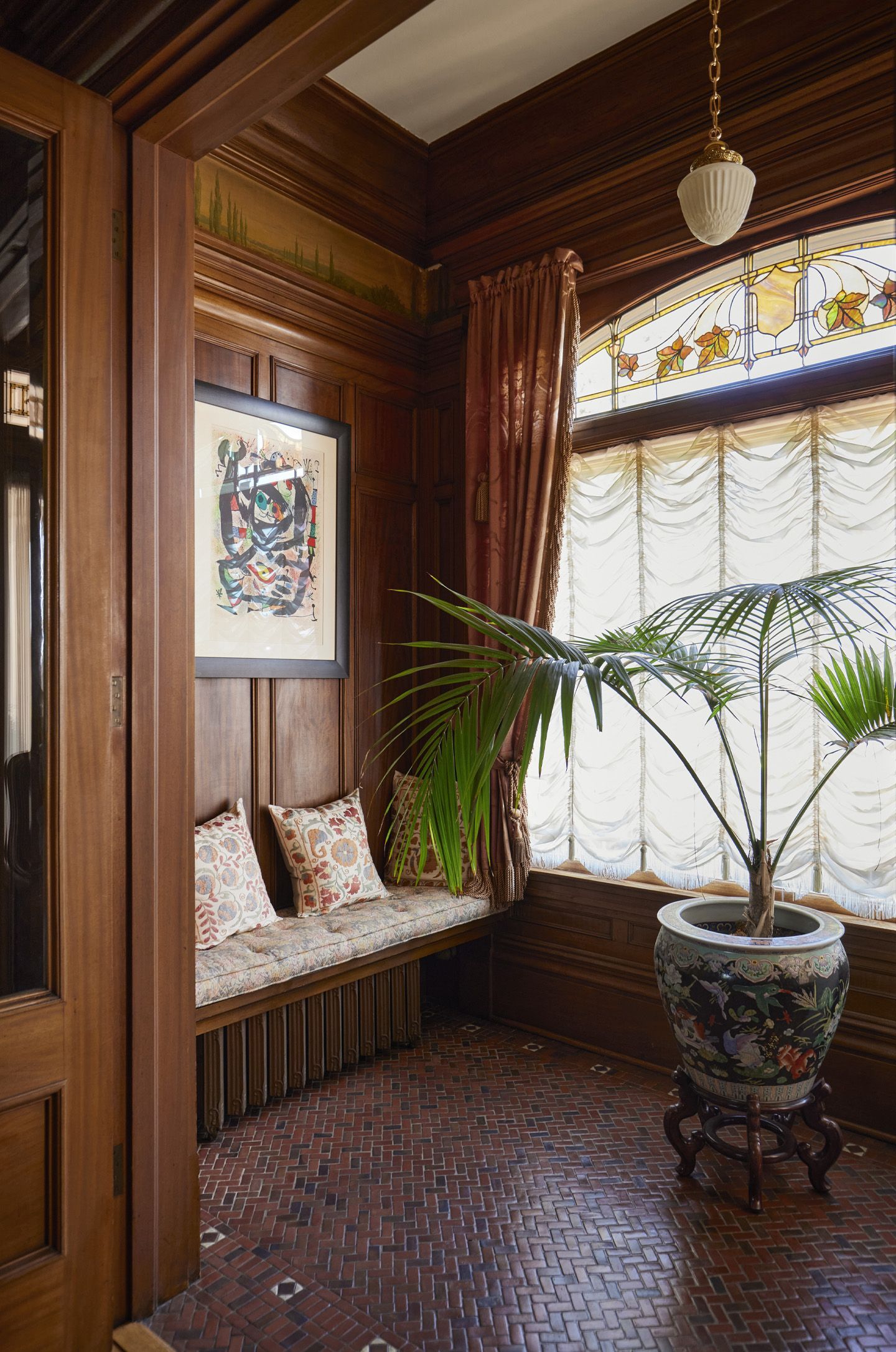 One of two sunrooms that flank the entry, with original floor mosaic tile, wall paneling painted frieze, built in bench seat with a large stained glass window facing the street.