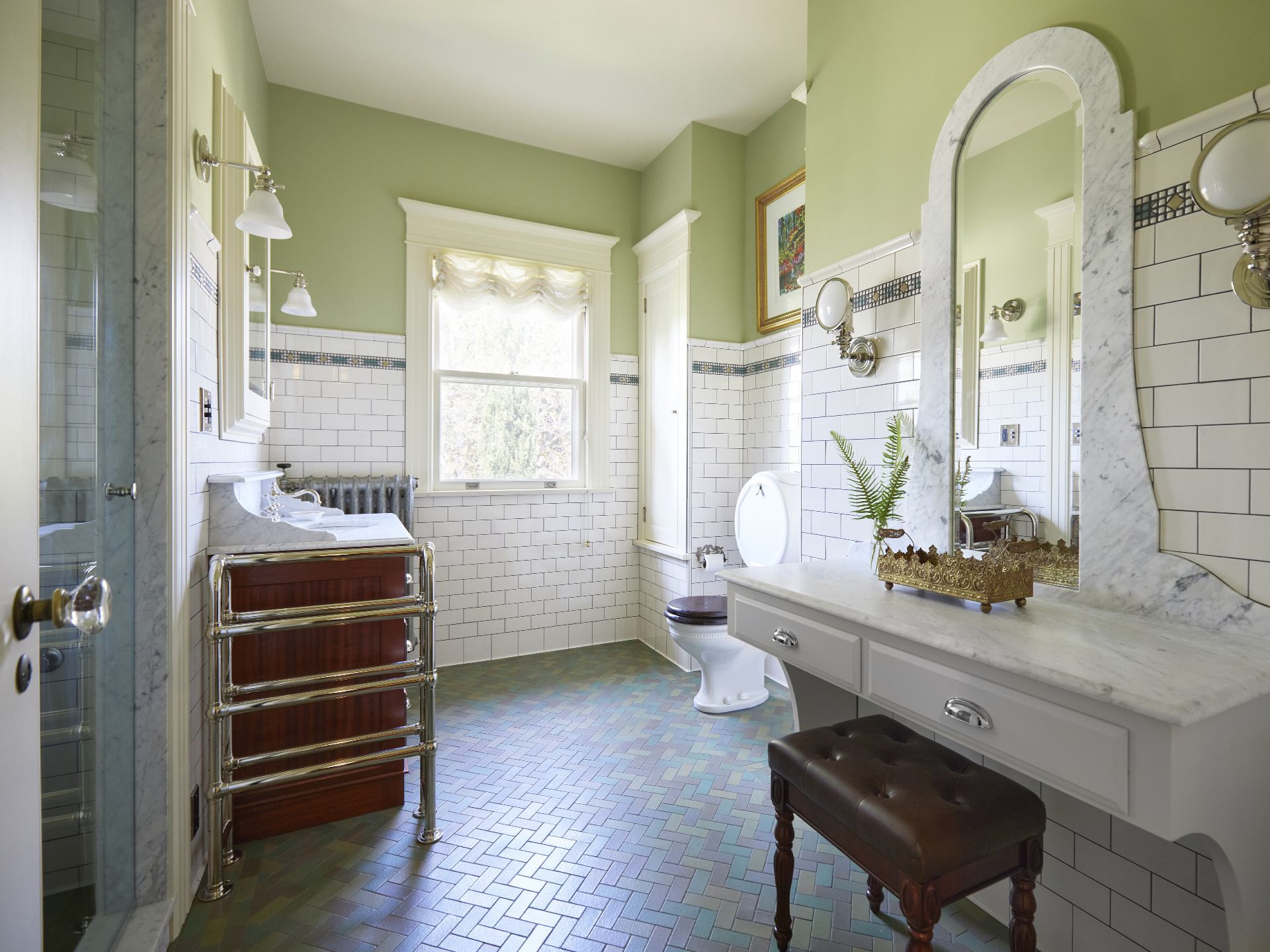 In the remodeled guest bath, the original pillbox toilet was restored. A makeup counter with marble top and mirror frame, floor mounted towel warmer, steam shower and new tile to match the old make this room feel like it was always there.