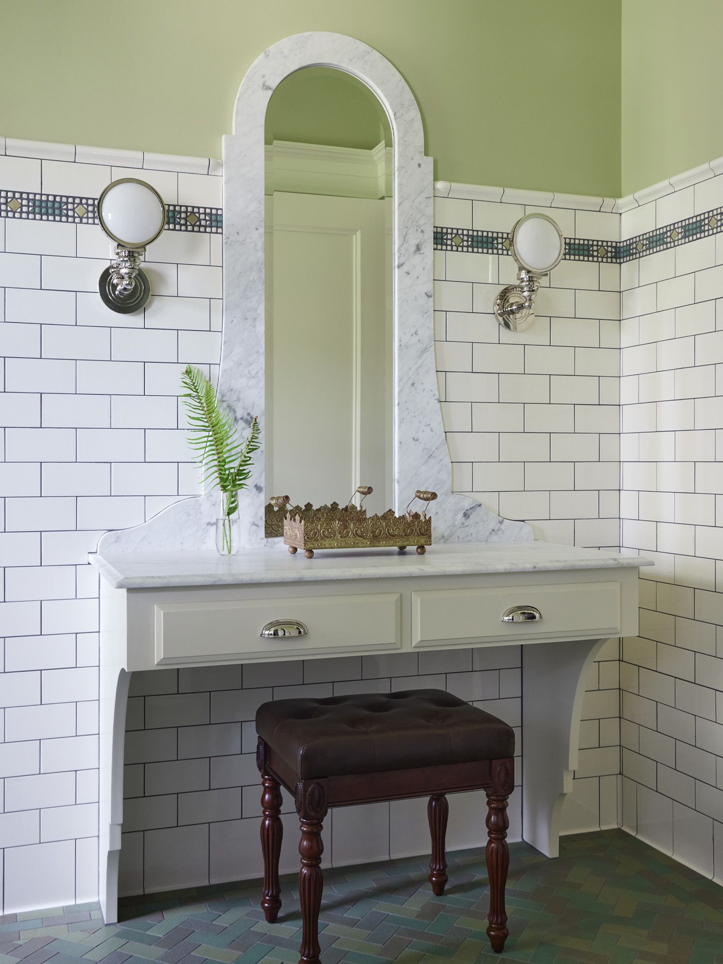 The makeup table, near the door, with tile wainscoting behind and a pair of sconces for illumination.