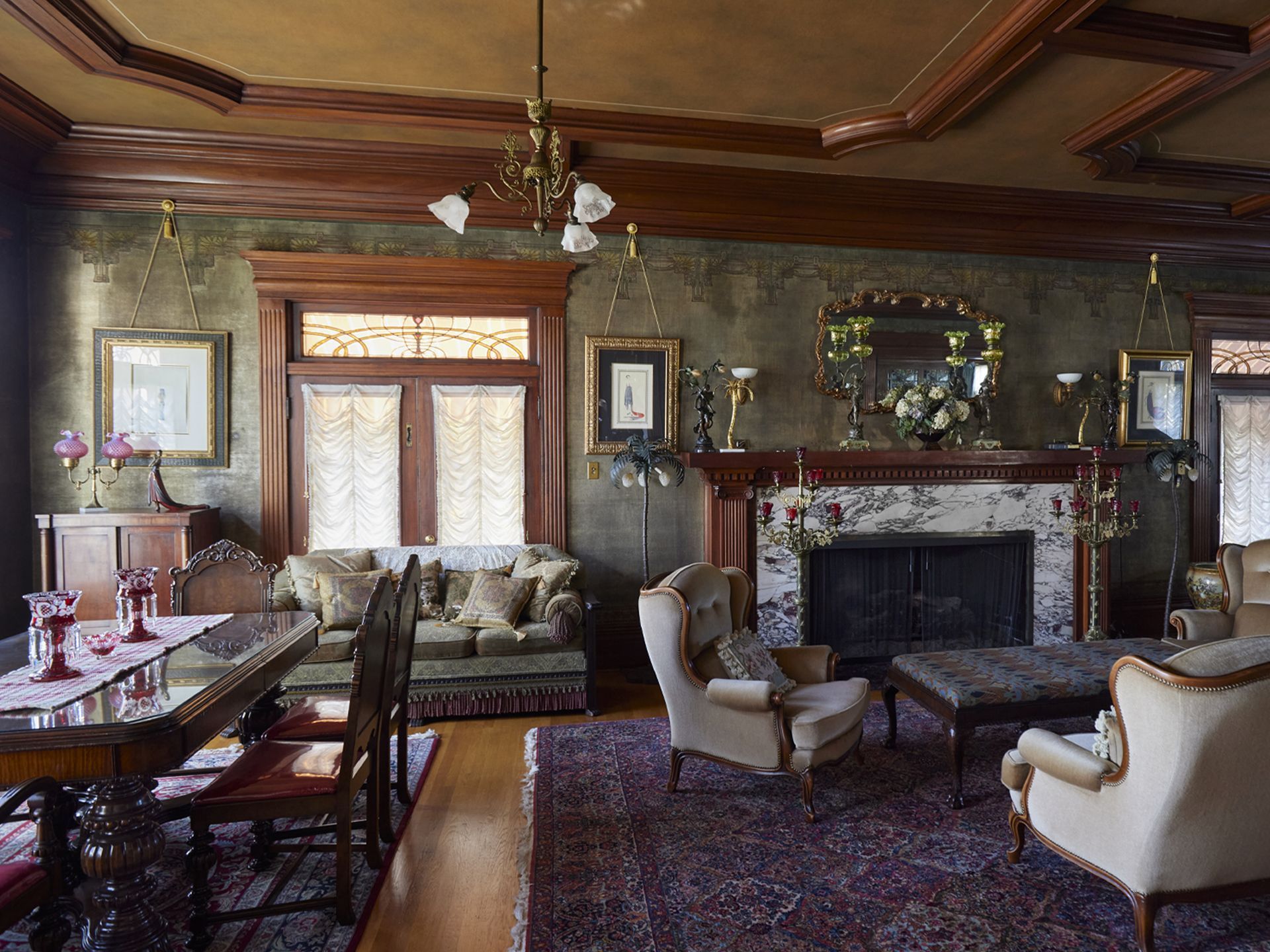 The living room with plentiful seating surrounding the original fireplace with original wallpaper, millwork and stained glass windows.