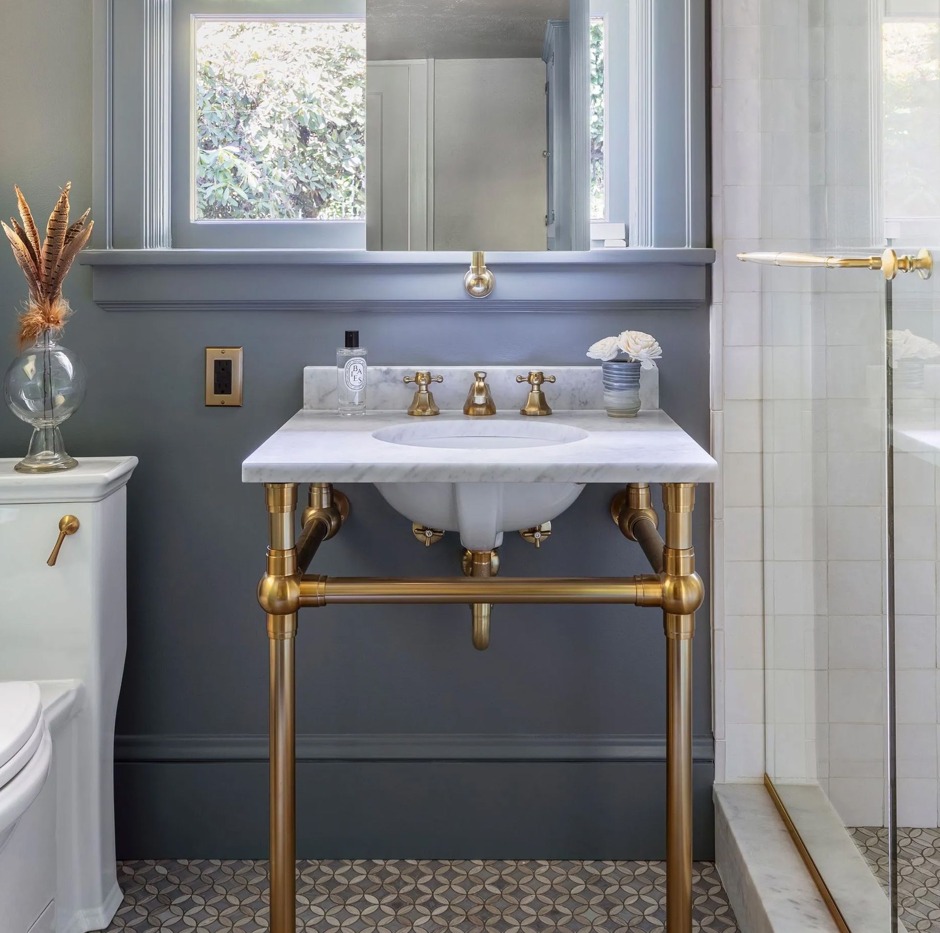 Original window placement is one of the biggest challenges in remodeling a vintage bath. In this case, a mirror mounted over the sash on brass hardware accommodates the placement of the sink directly below. 