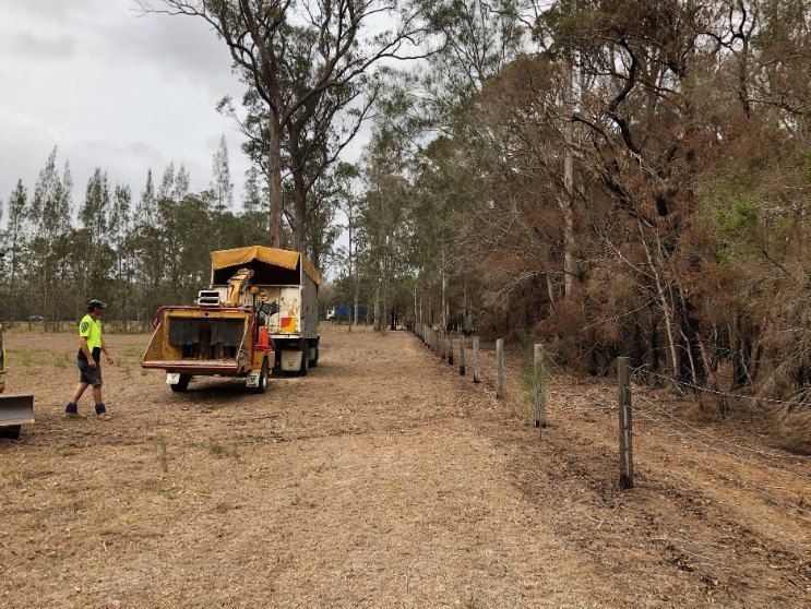 A Man is Standing Next to a Truck in a Dirt Field — Jeff Pearce Tree Services in Nabiac, NSW