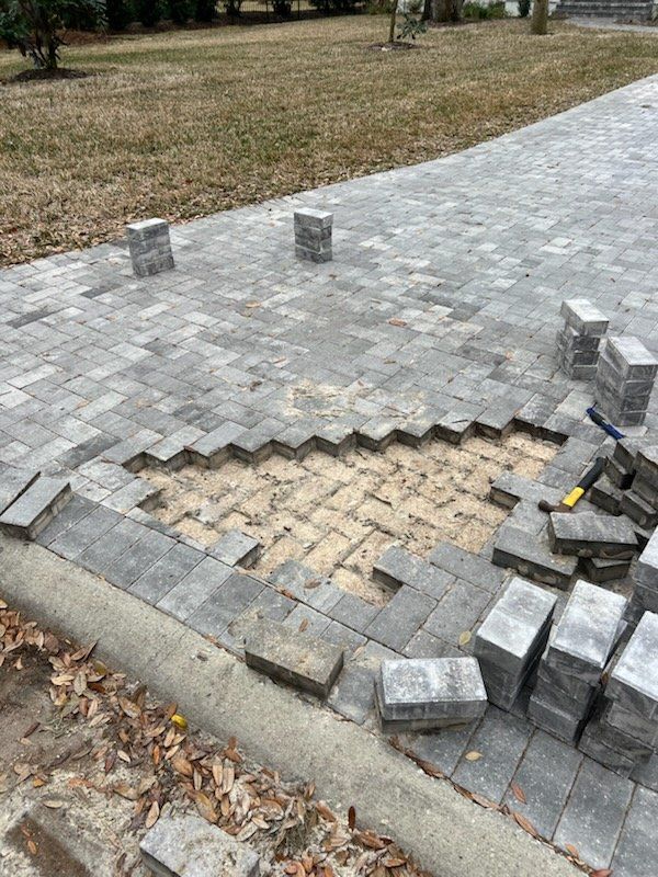 Pathway under construction: gray pavers being laid, exposing sand base near a curb.