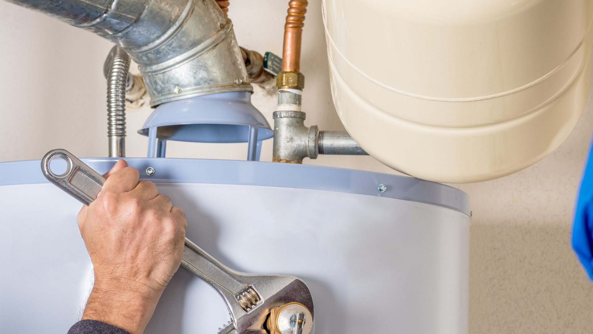 A man is fixing a water heater with a wrench.
