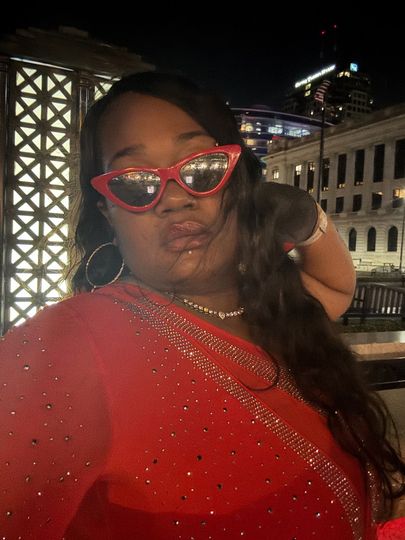 A woman in a red dress and red sunglasses is taking a selfie.