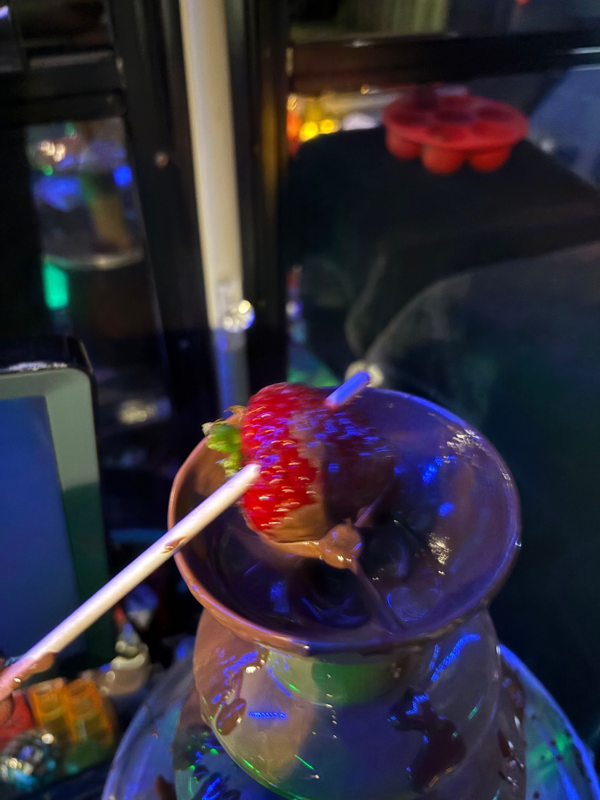 A person is dipping a strawberry into a chocolate fountain.