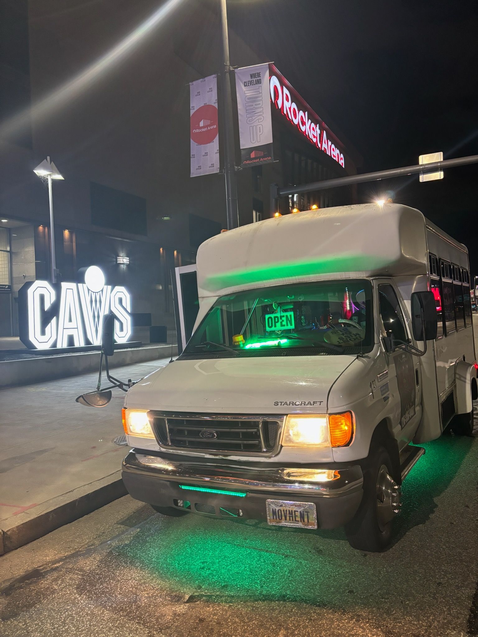 A white van with green lights on the front is parked in front of a cavs sign.
