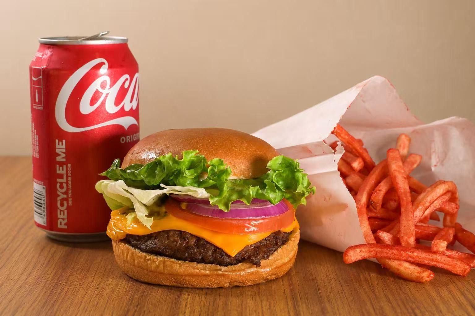 Burger, fries, and a Coca-Cola can on a wooden table.