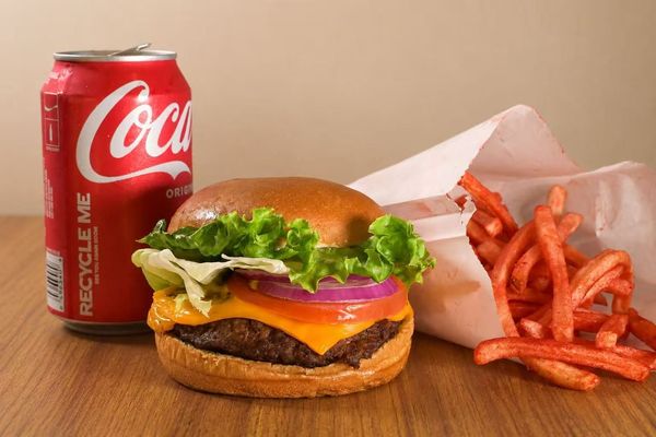 Burger, fries, and a Coca-Cola can on a wooden table.