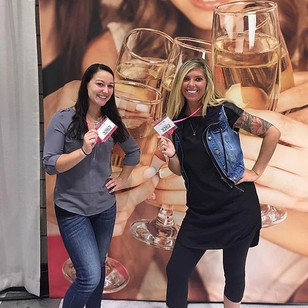 Two women standing in front of a picture of a woman holding wine glasses