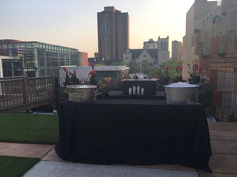 A table with a black table cloth is sitting on a patio with a city in the background.
