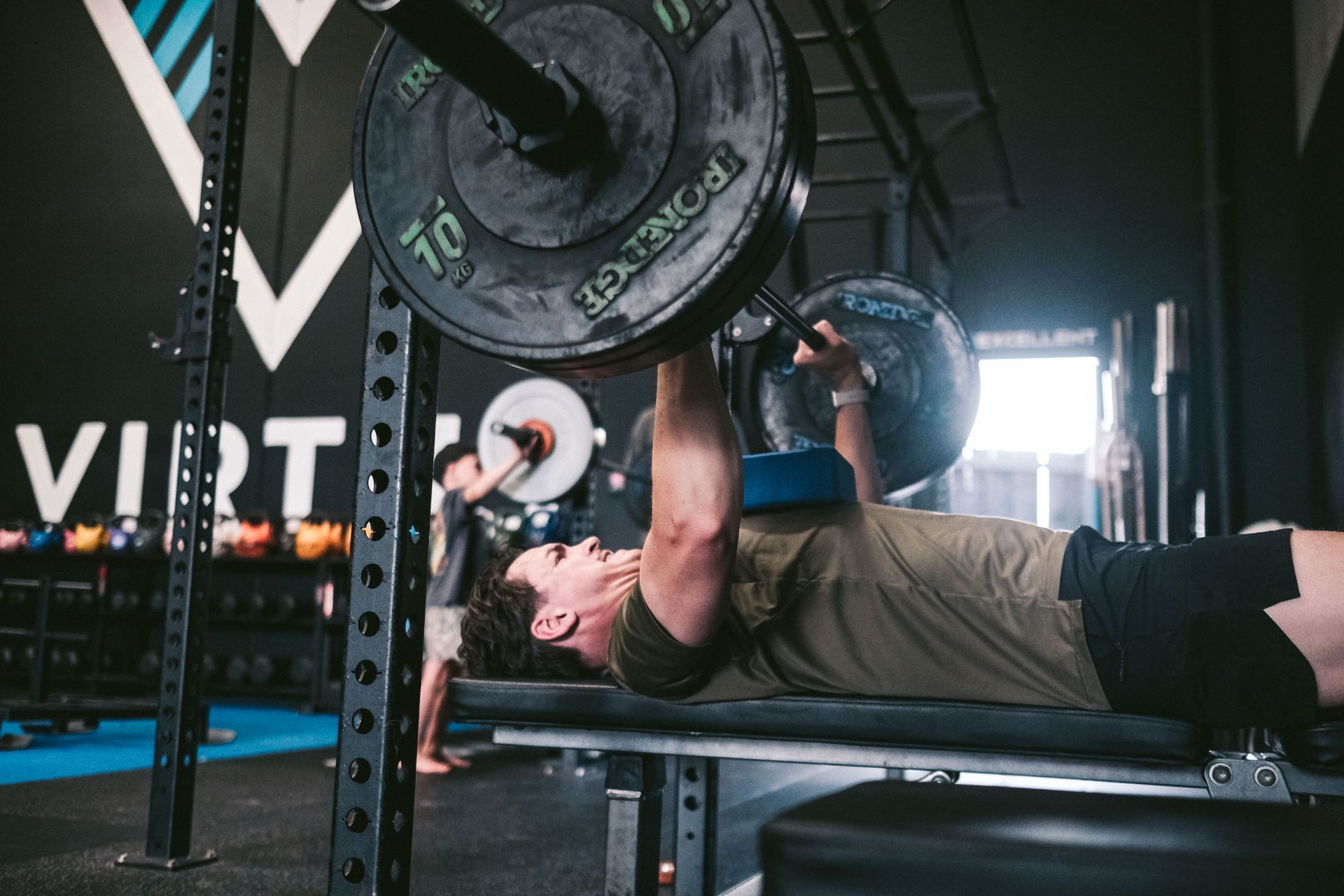 Man bench pressing weights with blue pad at gym.