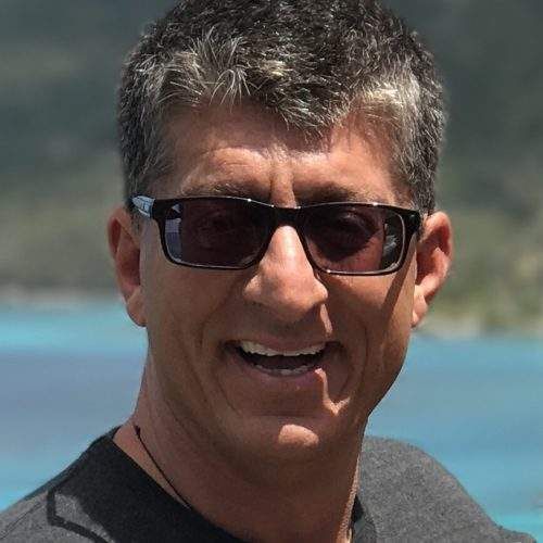 Man wearing sunglasses smiles outdoors, ocean background.