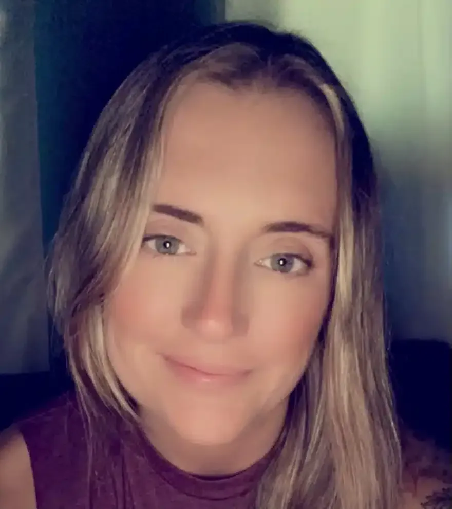 Woman with blonde hair smiles, wearing a maroon top.