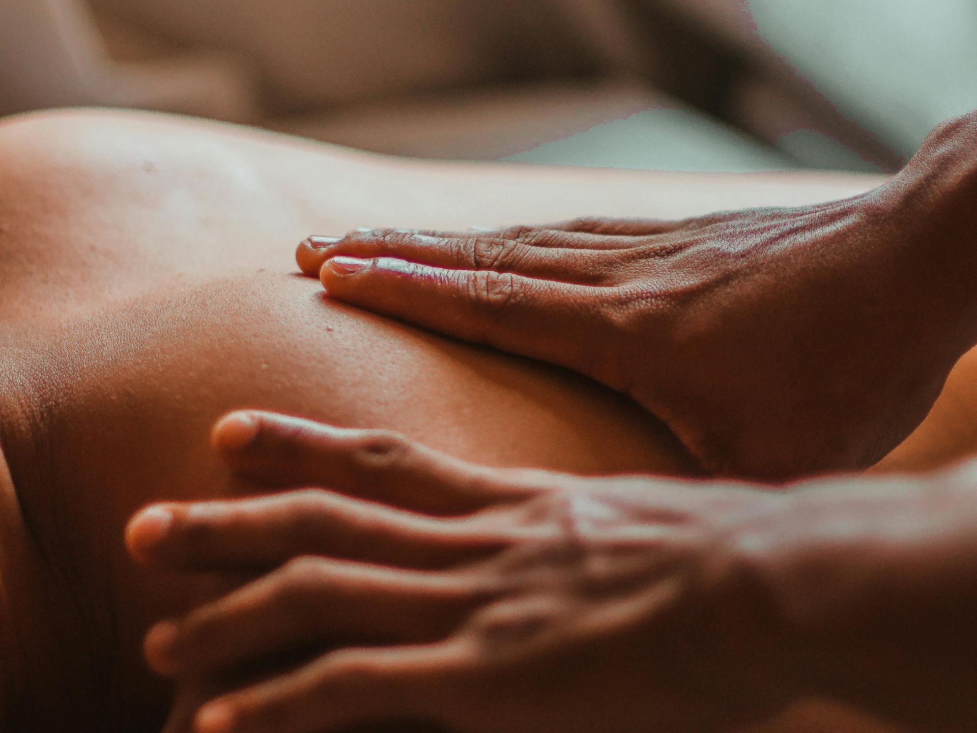 Hands giving a back massage. Dark skin tone, close-up. Oil glistens on skin.