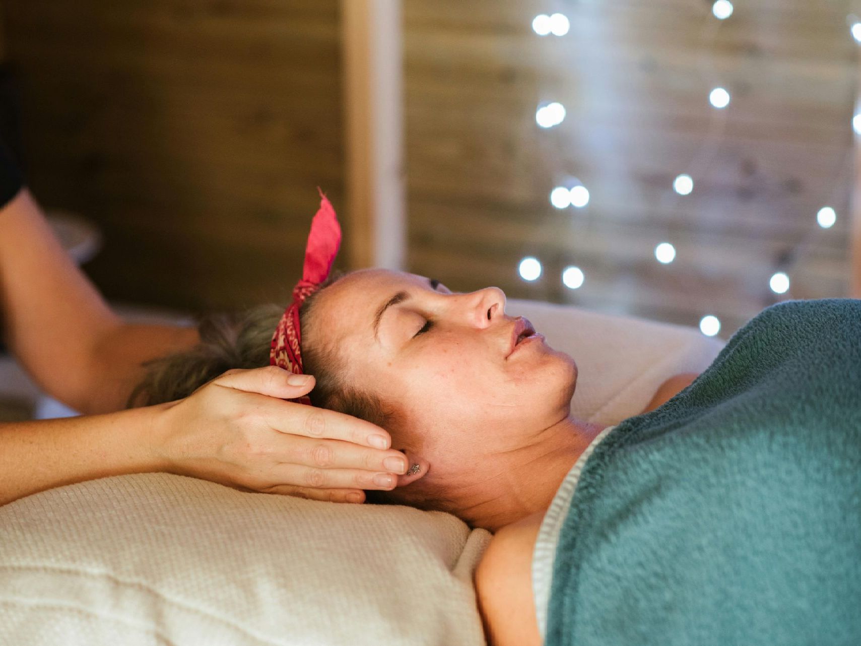 Woman receiving head massage, eyes closed, wearing red headband, in relaxing spa.