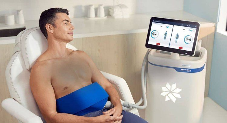 A shirtless man is sitting in a chair in front of a machine.