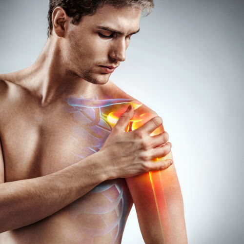 A shirtless man is holding his shoulder in pain.