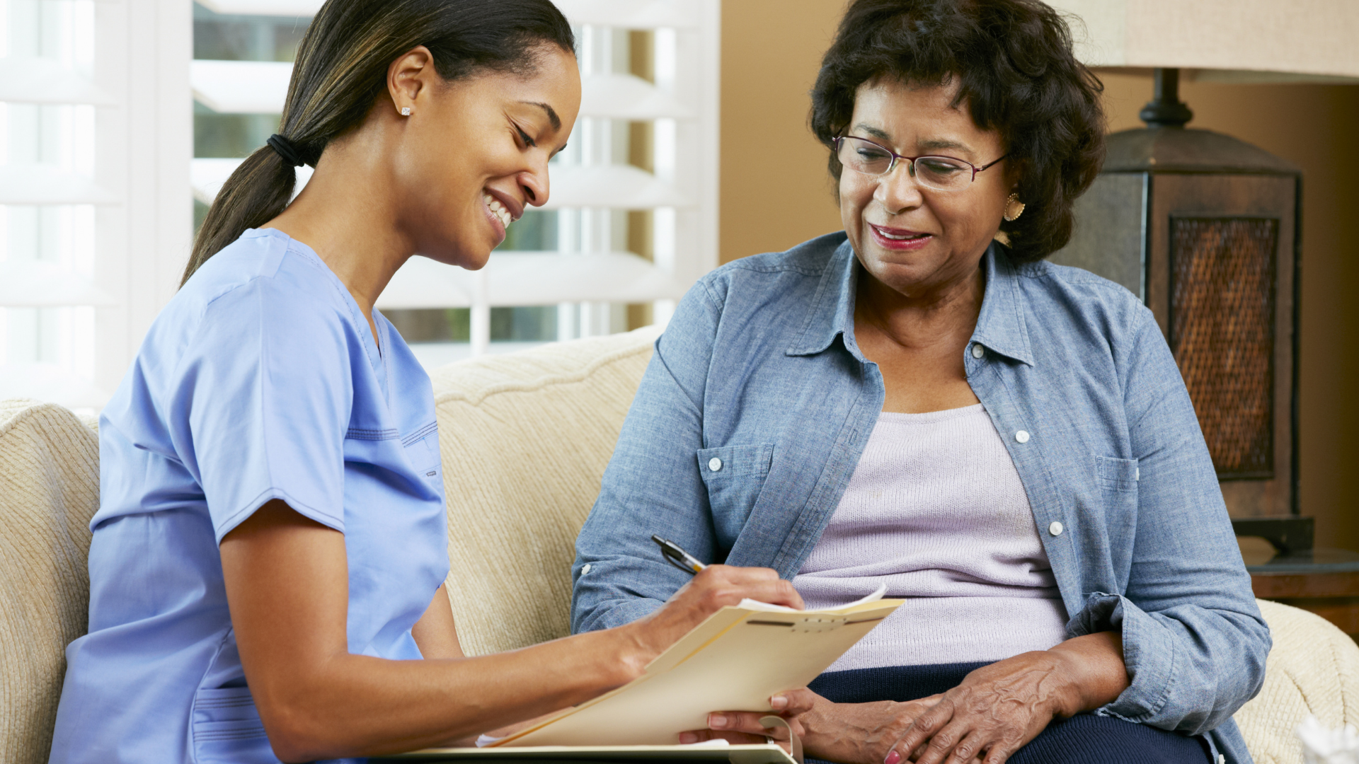 A nurse is talking to an elderly woman who is sitting on a couch.