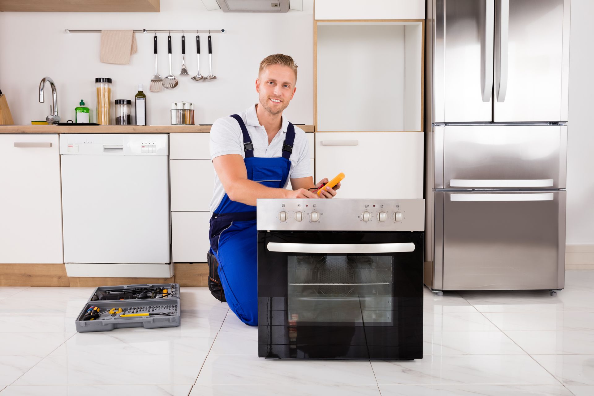 A man is kneeling on the floor fixing an oven in a kitchen.