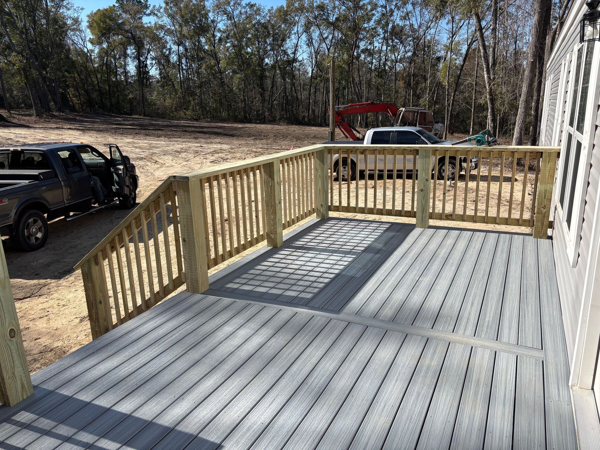 A gray deck with a wooden railing and a truck parked in the background.