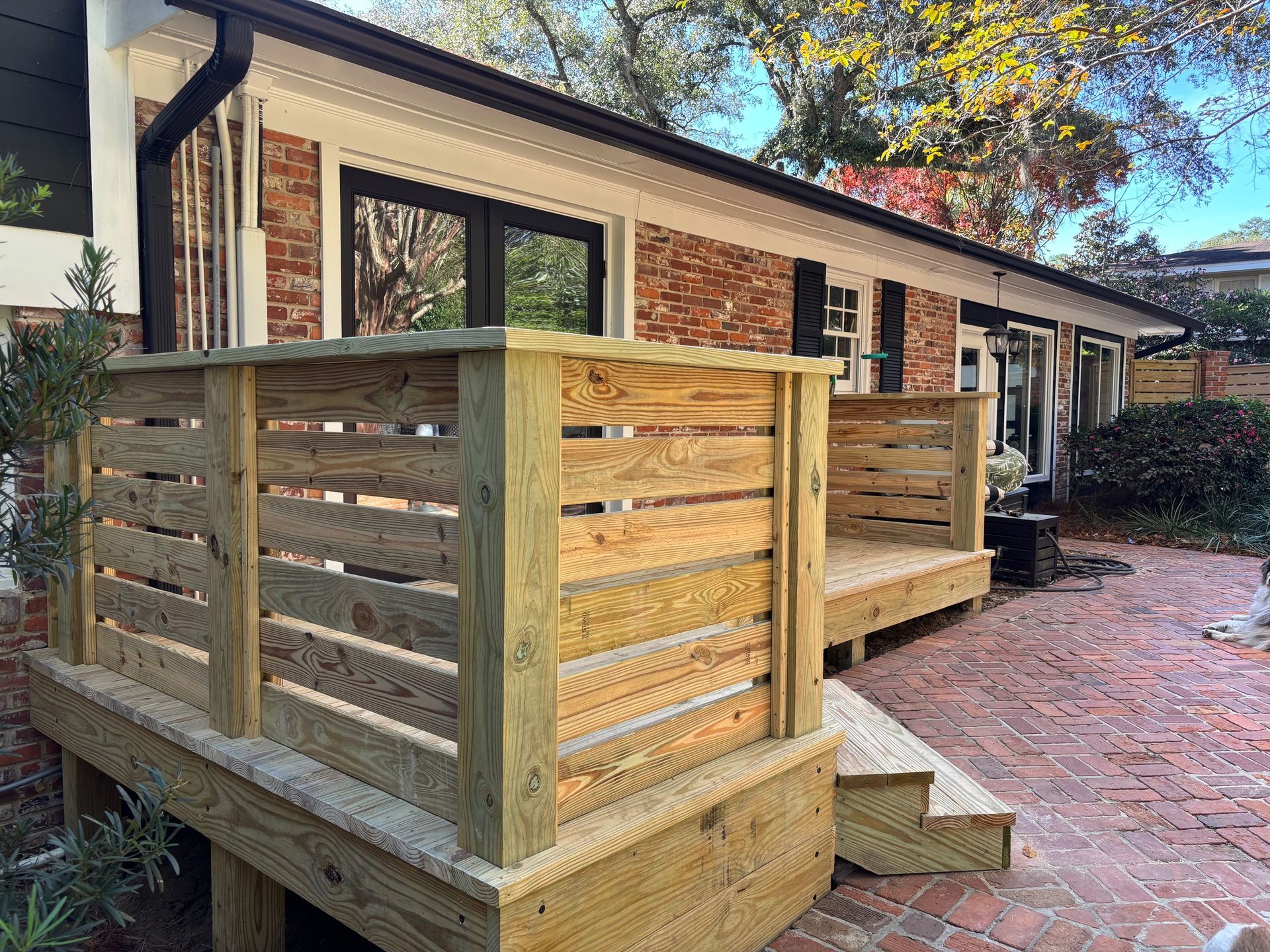 A wooden deck is sitting in front of a brick house.