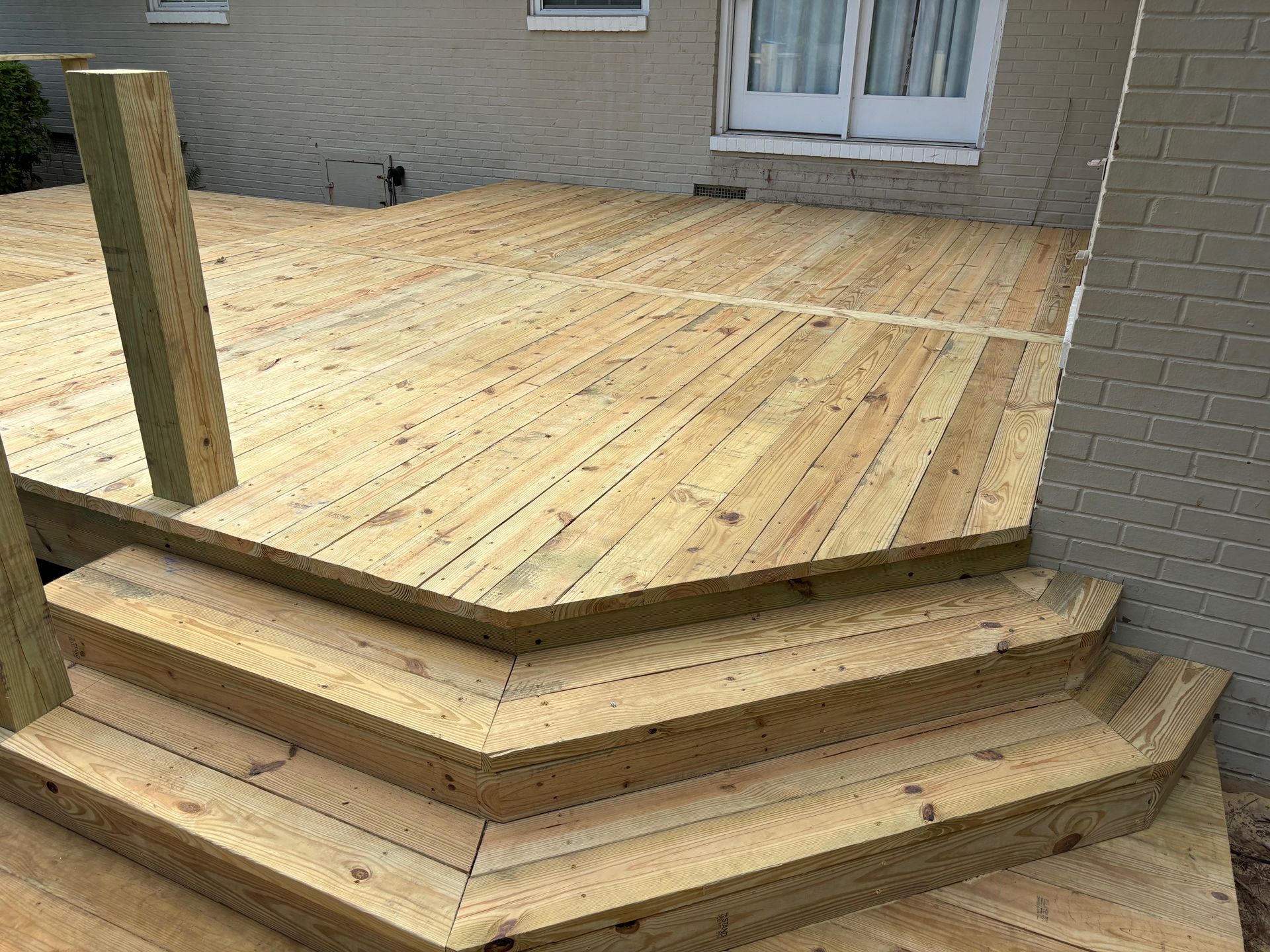 A wooden deck with stairs leading up to it and a brick building in the background.