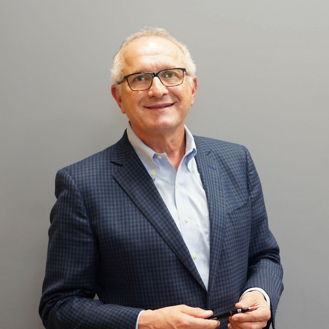 A man in a suit and glasses is smiling and holding a cell phone.