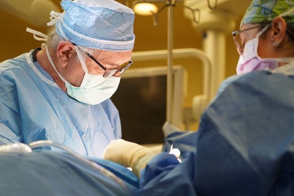 Dr. Ram Kalus, wearing a mask and gown, is operating on a patient.