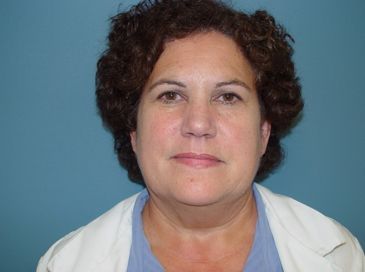 A woman with curly hair is wearing a white coat and a blue shirt.